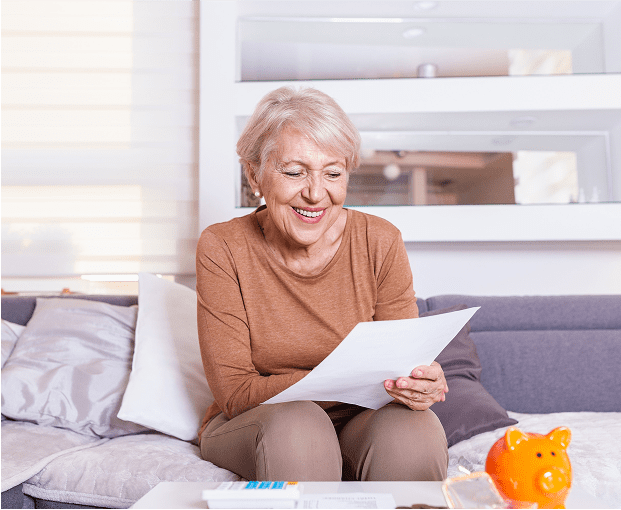 Elderly woman reading paper, smiling at home.