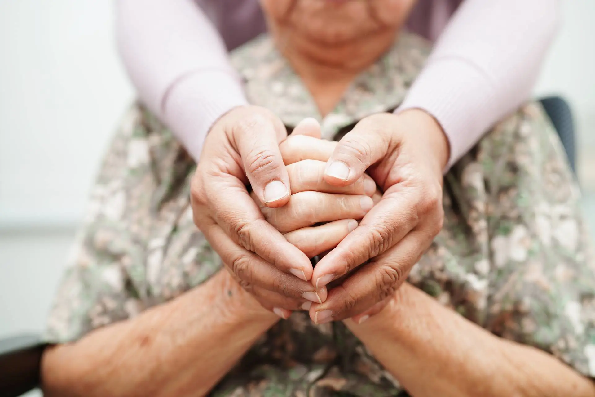 Hands of an elderly person gently held by a younger person.