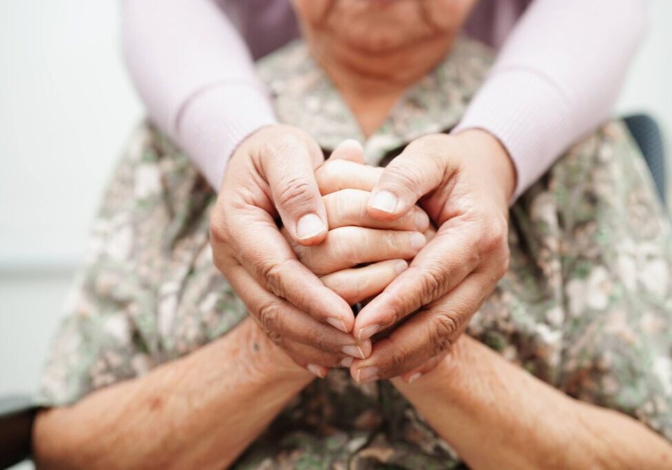 Hands of an elderly person gently held by a younger person.